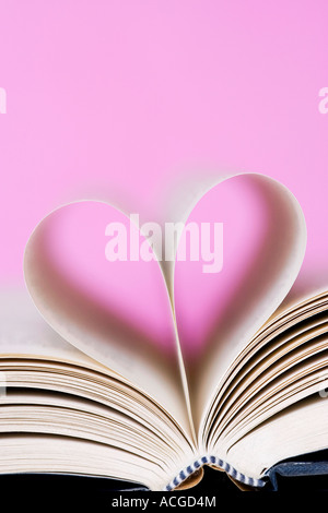 Forma di cuore costituito da pagine di libri contro un sfondo rosa Foto Stock