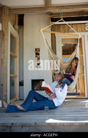 Una donna di lettura in un'amaca e un uomo di lettura sul pavimento su un patio. Foto Stock