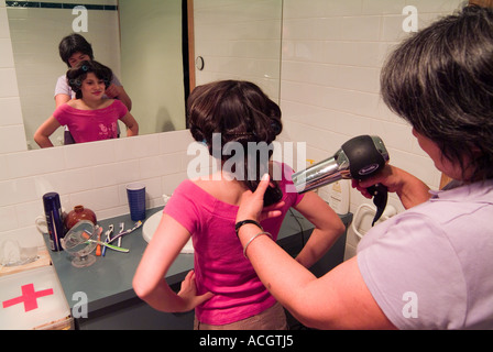 Una bambina di nove anni che si prepara per una festa davanti a uno specchio con la madre che si sta acchierando i capelli Foto Stock