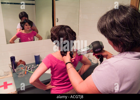 Una bambina di nove anni che si prepara per una festa davanti a uno specchio con la madre che si sta acchierando i capelli Foto Stock