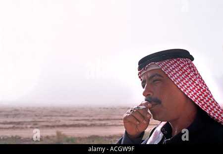 Giordano per uomo che indossa una keffiyah un tradizionale araba velo e fumare una sigaretta Wadi Rum Giordania Foto Stock