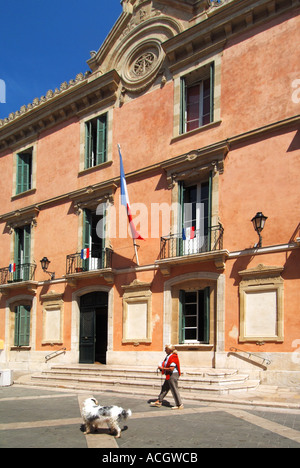 Camminatore di cane passando i passi fino all'ingresso e la soleggiata façade di St Tropez municipio edificio in Provenza-Alpi Côte Azzurra sulla Costa Azzurra Francia Foto Stock