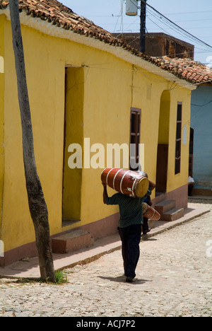 Gli uomini che trasportano i tamburi sulle loro spalle lungo una strada di ciottoli, Trinidad, Cuba. Foto Stock