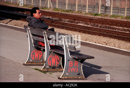 Un uomo seduto su una panchina ferroviaria che mostra sia GWR e BR badges Foto Stock