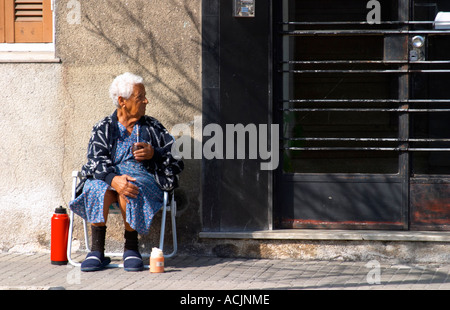 Una vecchia donna seduta sul marciapiede bevendo mate tè alle erbe, con un rosso caldo thermos thermos di acqua nella parte anteriore di un nero cancello di ferro porta. Montevideo, Uruguay Sud America Foto Stock