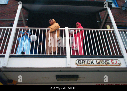 Le donne del Bangladesh guardando fuori dal loro balcone affacciato Brick Lane a Whitechapel est di Londra. Foto Stock