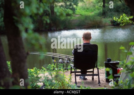 Un pescatore con tre aste seduto di fronte ad un lago a metà estate Foto Stock