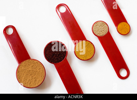 Rosso Cinque misurini da un cucchiaio per un quarto di cucchiaino di riempito con spezie su uno sfondo bianco Foto Stock