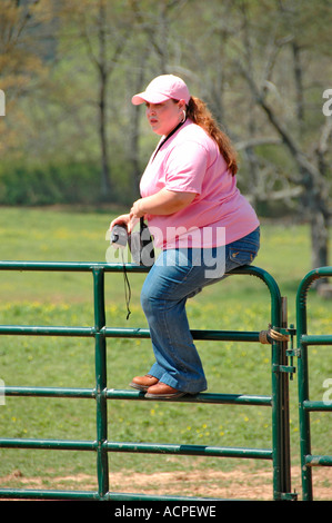 Molto grande donna sulla recinzione al dude ranch nel paese guardando roundup di bestiame da cowboy Foto Stock