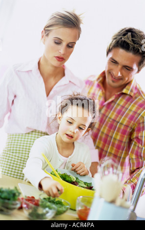 I genitori a guardare la figlia (6-7) preparare insalata Foto Stock