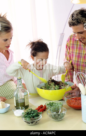 I genitori a guardare la figlia (6-7) preparare insalata Foto Stock