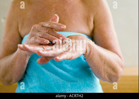 Senior donna avvolta in un asciugamano di applicare una lozione in mani, metà sezione, close-up Foto Stock