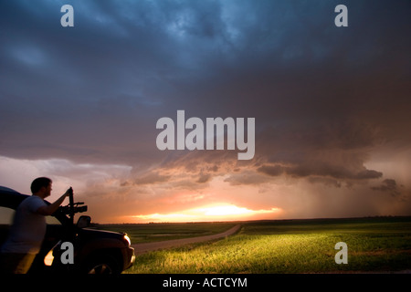 A Storm Chaser stagliano contro un grave supercell temporale nella centrale di Kansas al tramonto. Foto Stock