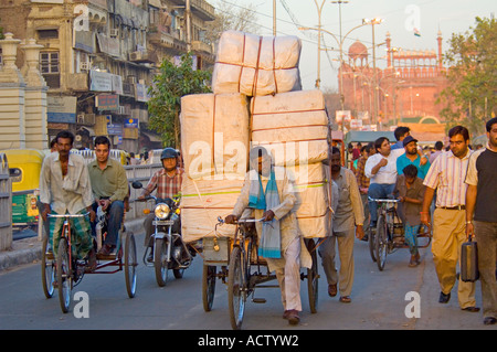 Scena di strada lungo Chandni Chowk con un ciclo di overload rickshaw in primo piano e il Forte Rosso (Lal Qila) in background. Foto Stock