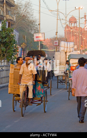 Scena di strada lungo Chandni Chowk con un ciclo risciò e passeggeri in primo piano e il Red Fort (Lal Qila) dietro. Foto Stock