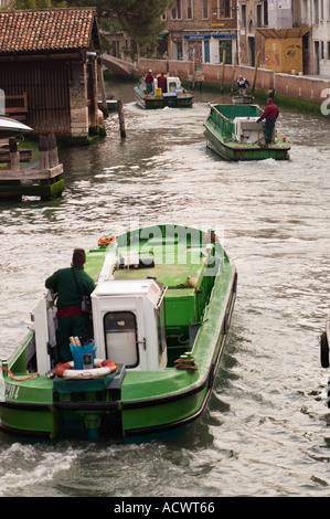 Tre green garbage barche sul loro modo di lavorare verso il basso un canale occupato a Venezia Italia Foto Stock