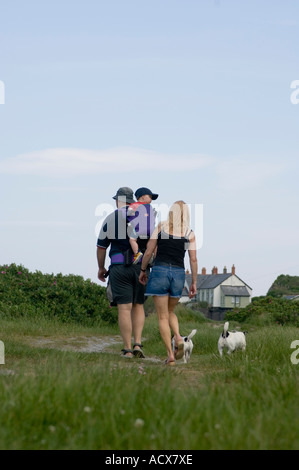 Giovane con bambino nello zaino a piedi con due cani di piccola taglia, giorno di estate Foto Stock