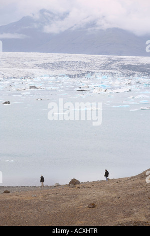 Due persone che camminano sulla riva del Jokulsarlon laguna glaciale, ghiacciaio Vatnajokull in Islanda Foto Stock