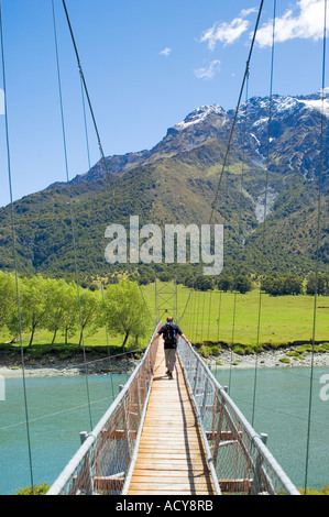 Maschio singolo escursionista attraversa la sospensione ponte sul fiume Matukituki in Mount aspiranti National Park, Nuova Zelanda Foto Stock