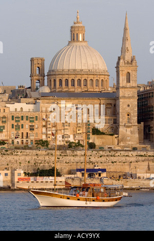 Yacht che naviga oltre la Valletta al tramonto. Vista ravvicinata che mostra la cupola della chiesa e il campanile. Foto Stock