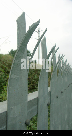 Sharp picchi di curva sulla sommità di un muro di sicurezza lungo il lato di una linea ferroviaria. Foto Stock