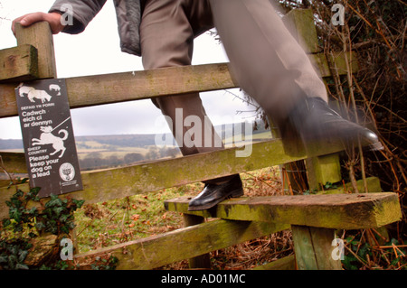 Un pensionato uomo passi attraverso uno stile di legno con un VI PREGHIAMO DI CONSERVARE IL VOSTRO CANE SU UN SEGNO DI PIOMBO NEI PRESSI DI ABERGAVENNY Wales UK Foto Stock