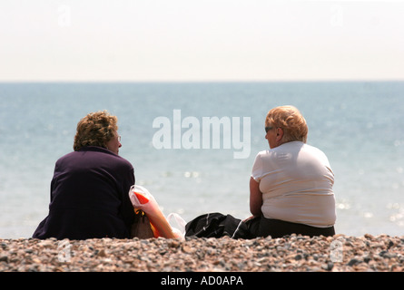 Donne di mezza età seduti sulla spiaggia di ciottoli di calore estivo Foto Stock