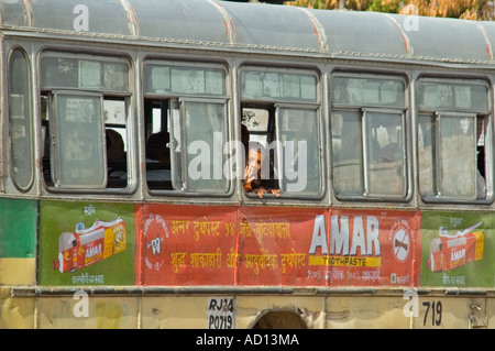 Vista orizzontale di un piccolo ragazzo indiano sventolare dalla finestra di un vecchio traballanti bus pubblico nel centro di Delhi. Foto Stock