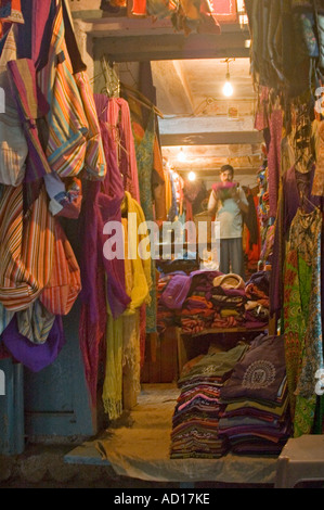 Vista verticale al di fuori di un oscuro tessuti indiani negozio con merce esposta al di fuori, giù un vicolo di Varanasi Foto Stock