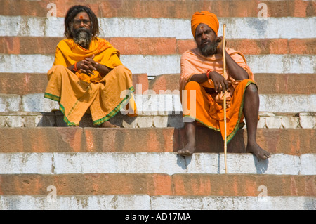 Chiudere orizzontale di due Sadhus tradizionalmente condita in arancione seduto su Kedar Ghat lungo il fiume Gange. Foto Stock