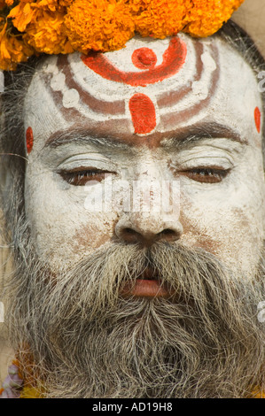 Close up ritratto di un sadhu (holyman) decorato con orange ghirlande di fiori si siede in preghiera presso uno dei ghats di Varanasi. Foto Stock