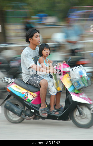 Fratello e Sorella di giovani accelerando su una motocicletta per le vie di Lopburi Thailandia Foto Stock