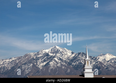 Una chiesa bianca steeple nella Salt Lake Valley, Utah, Stati Uniti d'America, con la coperta di neve montagne rocciose in background. Foto Stock