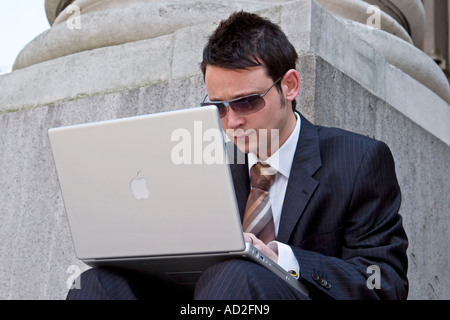 Giovane imprenditore guarda i dati finanziari sul suo laptop nella città di Londra Foto Stock