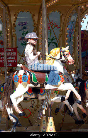 Giovane ragazza adolescente indossando vestiti alla moda a cavallo di una giostra cavallo Foto Stock