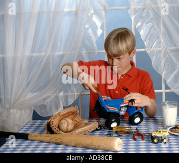 Industriosa giovane ragazzo la riparazione di uno dei suoi giocattoli in una cucina domestica impostazione della finestra Foto Stock