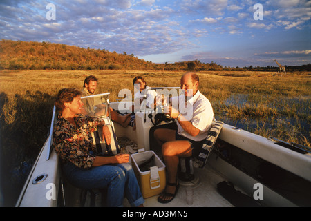 Le coppie aventi un drink al tramonto sul lago Kariba in Zimbabwe con giraffe e impala in distanza Foto Stock