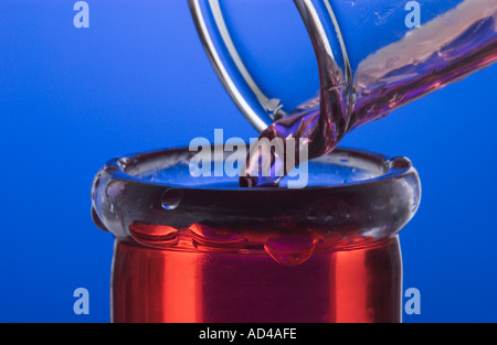 Rosso fluido che viene versata dal tubo di prova nella beuta di Erlenmeyer Foto Stock