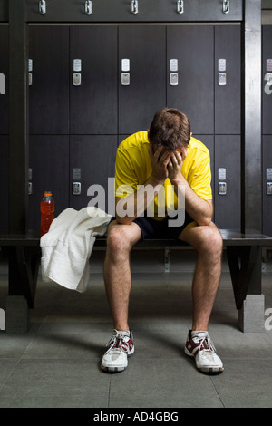 Un uomo seduto con la testa tra le mani in un Locker room Foto Stock