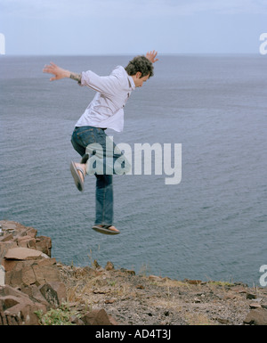Un uomo salta fuori da una scogliera vicino al mare Foto Stock