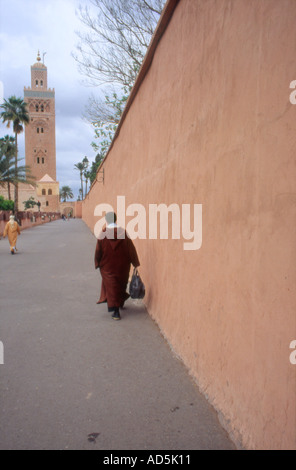 Donna che cammina lungo la parete con la moschea di Koutoubia in background Marrakech marocco Foto Stock