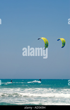 Verticale di ampio angolo di due kitesurfisti eseguendo spettacolari salti acrobatici fuori le cime delle onde in una giornata di sole. Foto Stock