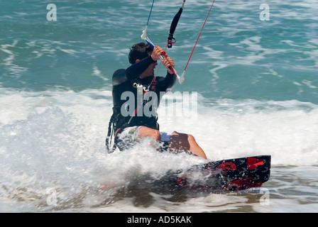 Chiudere orizzontale di un maschio caucasico kitesurfer in una posizione accovacciata schiantarsi attraverso le onde Foto Stock