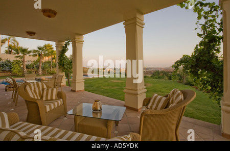 Poltrone in vimini e divano con crema e marrone e cuscini a strisce sulla veranda con vista di prato Foto Stock