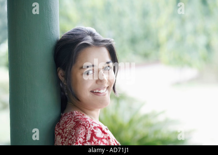 Ritratto di una giovane donna appoggiata contro un pilastro sorridente Foto Stock