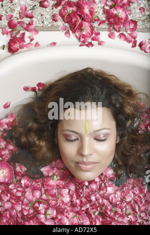 Ritratto di una giovane donna che giace in una vasca con petali di fiori galleggiante Foto Stock