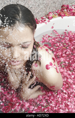 Close-up di una giovane donna in una vasca da bagno ricoperta con petali di fiori Foto Stock