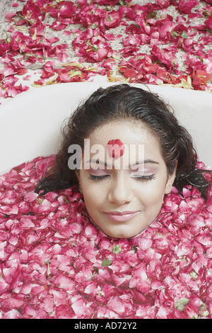 Ritratto di una giovane donna che giace in una vasca da bagno ricoperta con petali di fiori Foto Stock