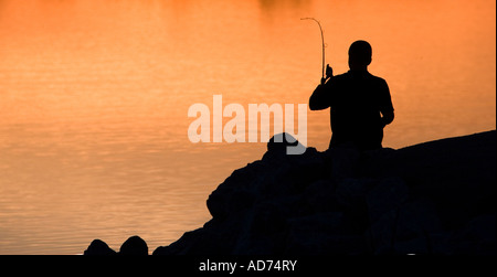 Una silhouette di un uomo la colata di una linea di pesca al tramonto. Foto Stock