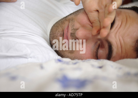 Giovane uomo disteso nel letto, svegliarsi, stropicciandosi gli occhi, close up Foto Stock